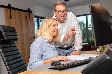 Olaf Memering und seine Mitarbeiterin stehen zusammen an einem Schreibtisch und besprechen etwas.